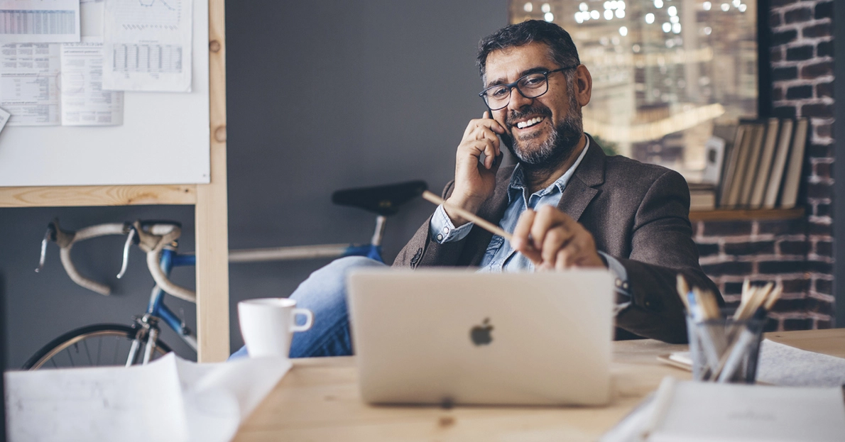 Ein Mann nutzt einen Apple Macbook während eines Anrufs im Büro