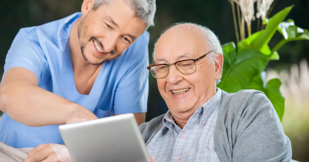 Pflegekraft unterstützt einen Senioren bei der Bedienung eines mobilen Tablets