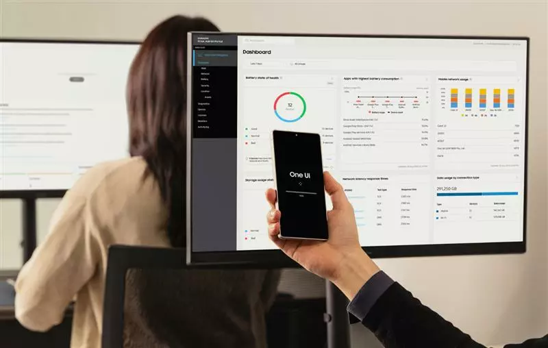 Knox Datensicherheit Person hält Smartphone vor Monitor auf dem Samsung Knox Manage geöffnet ist