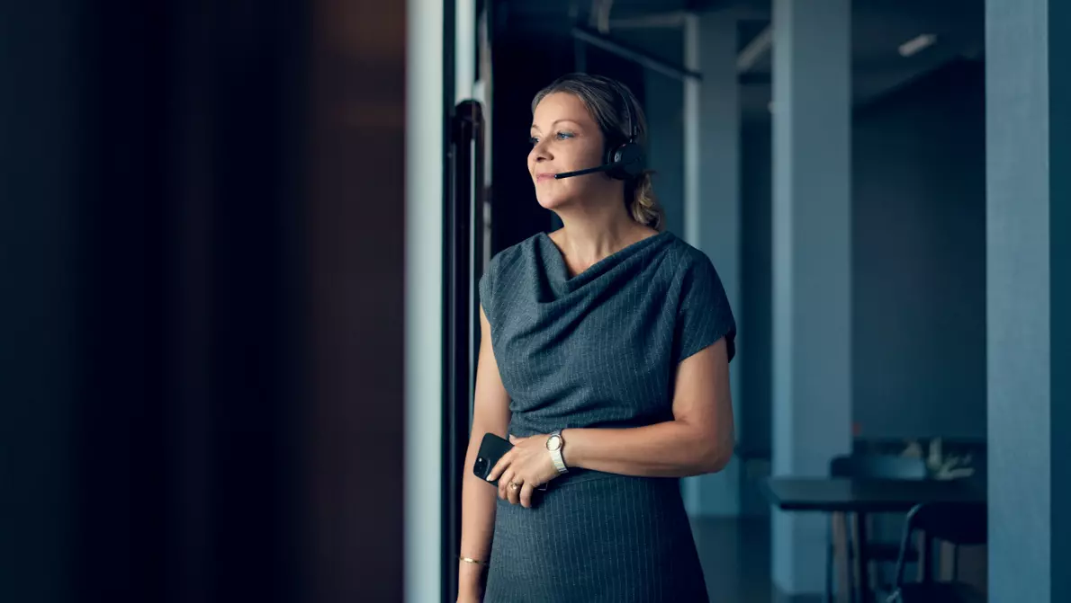 Frau schaut aus Fenster und trägt kabelloses Headset