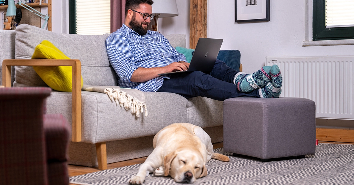 Ein Mann nutzt ein Apple MacBook auf Couch im Homeoffice