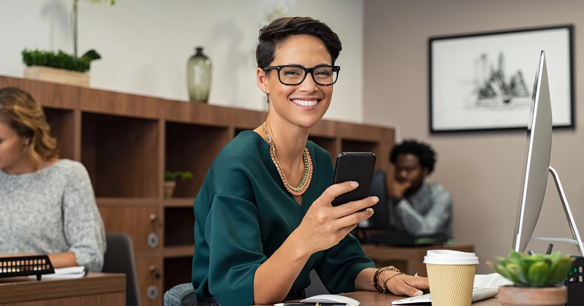 Eine Frau mit Smartphone lächelt am Arbeitsplatz
