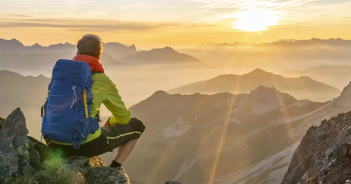 Mann sitzt auf einem Berggipfel und betrachtet den Sonnenuntergang