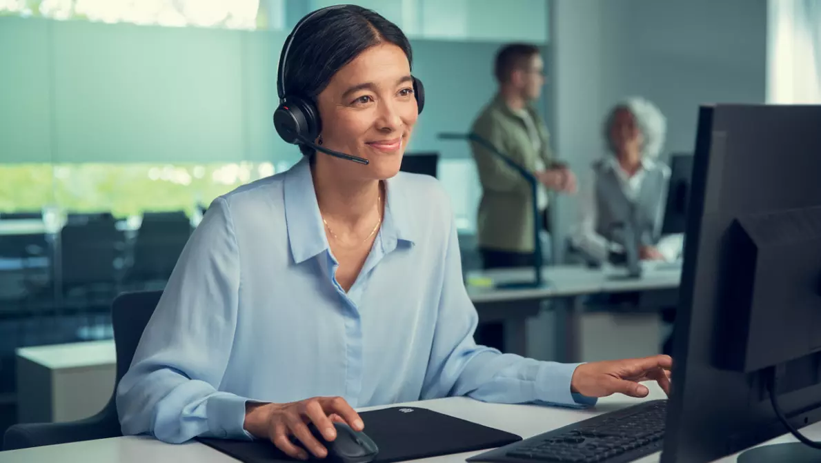 Frau in hellblauen Oberteil sitzt im Büro mit Wireless Headset