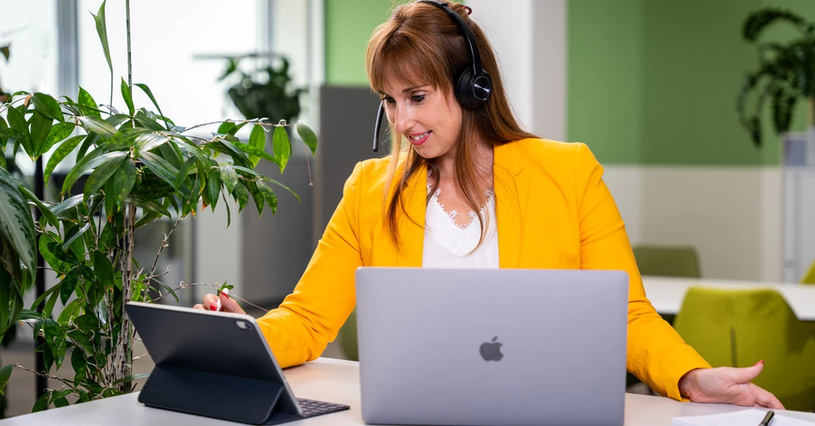 Eine Frau mit gelbem Blazer nutzt ein Apple Macbook am Arbeitsplatz